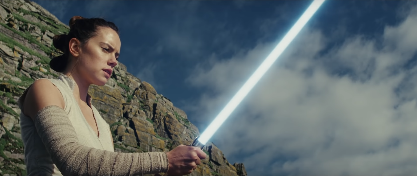 Rey looking at the blue lightsaber she's holding.